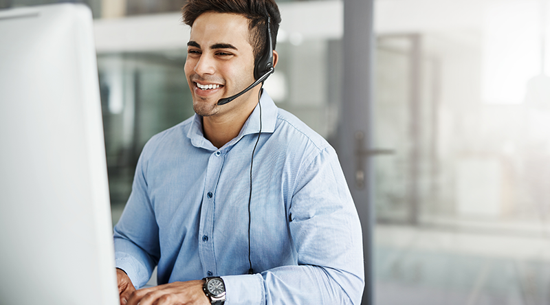 employee smiling and talking on headset while working on computer
