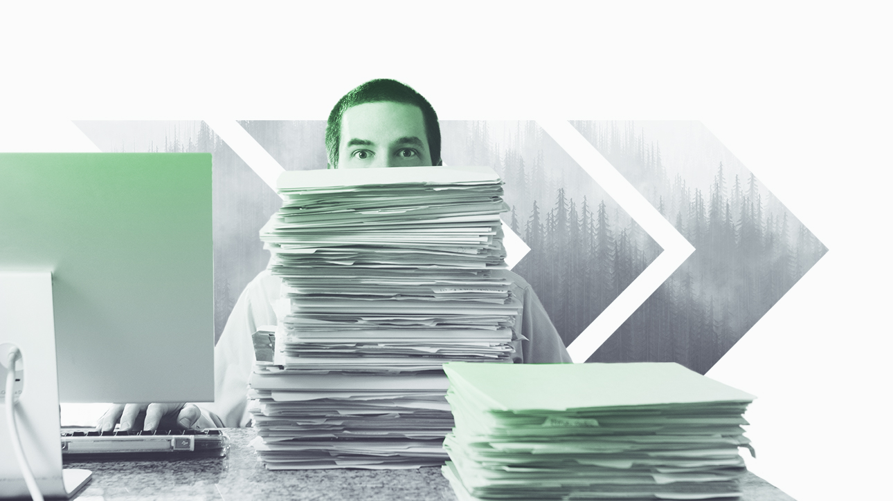 Male employee peeking over large stack of paperwork